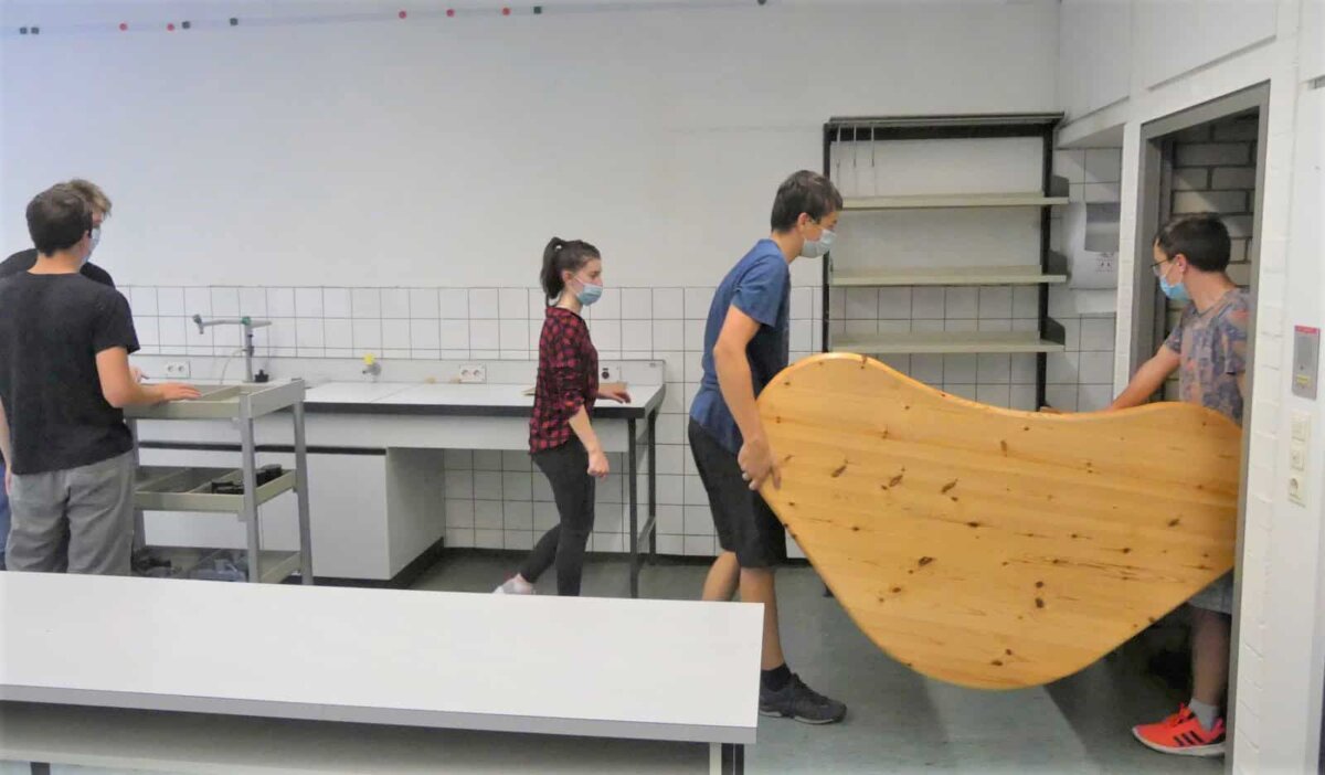 Alles muss raus: Schülerinnen und Schüler schaffen die Möbel aus dem Physikraum in ein  leeres Klassenzimmer