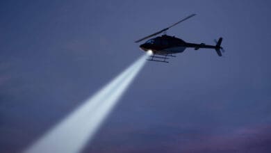 police helicopter shining a light beam in the dark sky