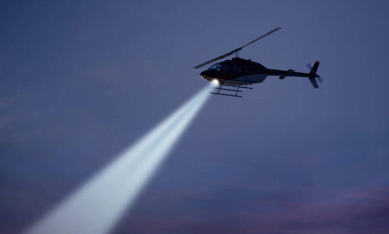 police helicopter shining a light beam in the dark sky
