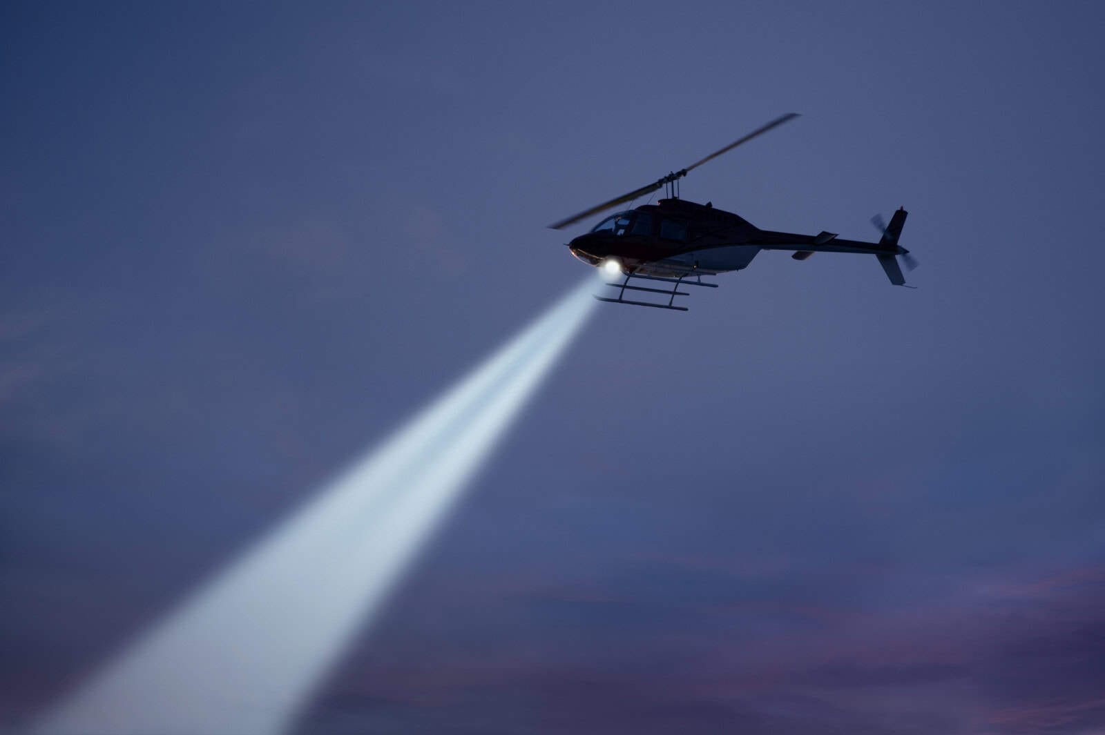 police helicopter shining a light beam in the dark sky