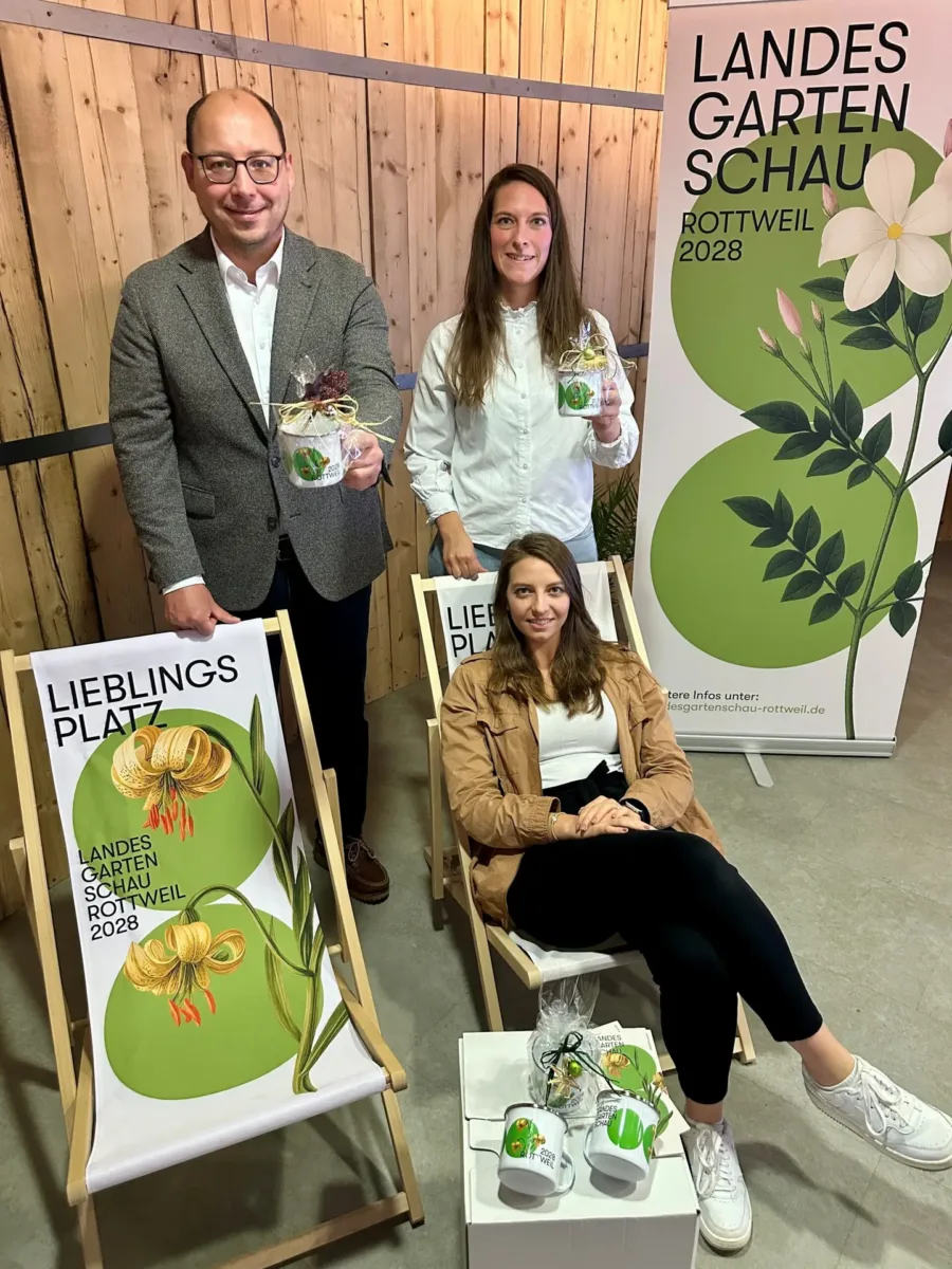 Oberbürgermeister Dr. Christian Ruf, Miriam Ruess (hinten) und Eileen Heber (vorne, beide LGS Rottweil 2028 gGmbH) freuen sich über den Verkaufsstart der frisch eingetroffenen Landesgartenschau-Tassen und Liegestühle (Foto: Stadt Rottweil / Hermann).
