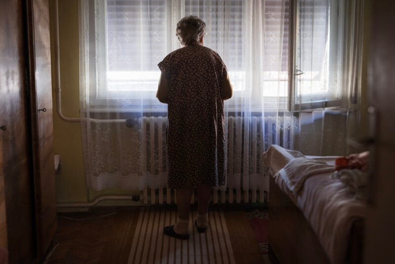 senior woman looking through window curtain