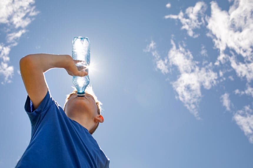 little boy drinking water from bottle on hot summer day.