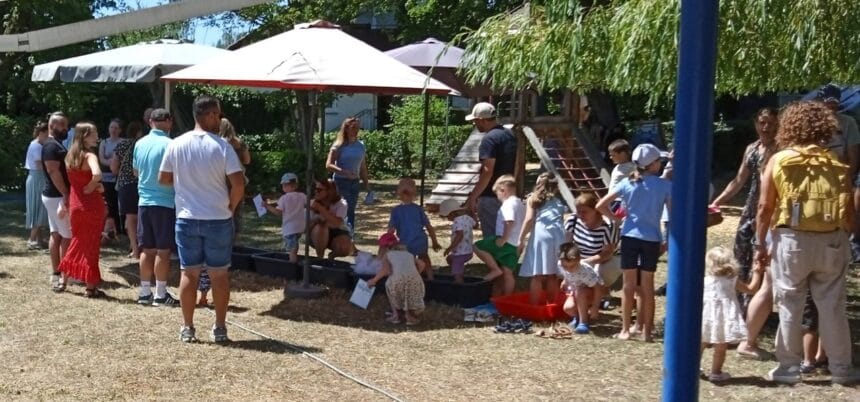 Eltern und Kinder genießen einen Sommertag im Park mit Spielen und Aktivitäten unter Sonnenschirmen.