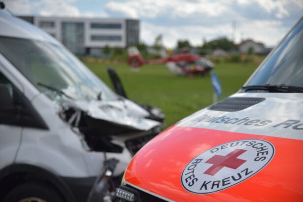 Rettungseinsatz mit Krankenwagen und Hubschrauber auf Wiese vor modernem Gebäude im Hintergrund.