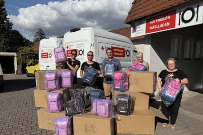 Menschen stehen vor Rottweiler Tafelladen mit gespendeten Schulranzen, gefüllt mit Schulsachen, bei sonnigem Wetter.