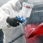 car painter sprays red color paint to part of vehicle using spray gun in workshop garage. complex repair and restoration automobile with exact select of color after accident.