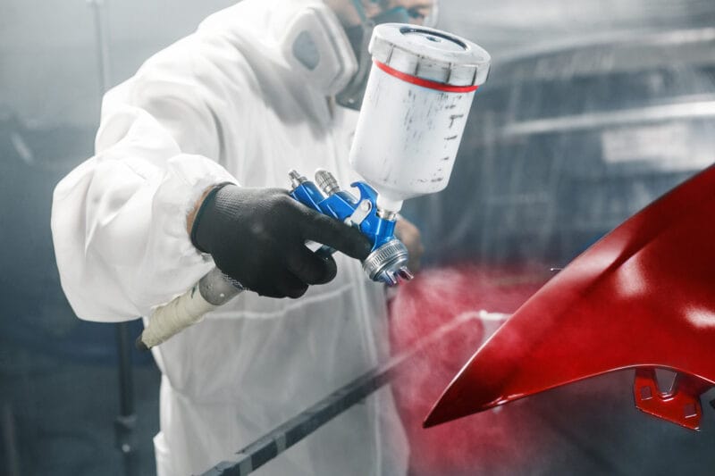 car painter sprays red color paint to part of vehicle using spray gun in workshop garage. complex repair and restoration automobile with exact select of color after accident.