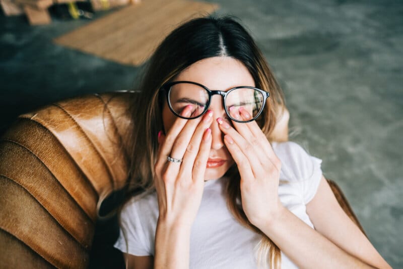 young woman rubs her eyes after using glasses. eye pain or fatigue concept.