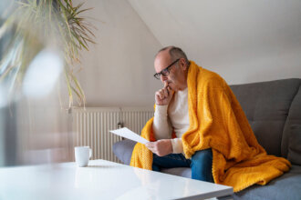 man with blanket reviewing heating bill on sofa at home